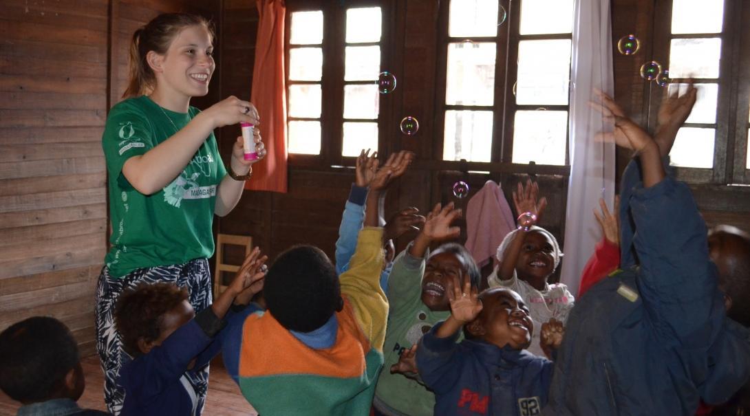 A female volunteer blows bubbles to a group of children trying to catch them during a kindergarten lesson at her Childcare Project in Madagascar. Projects Abroad volunteer with children in Madagascar blows bubbles for a group of children to catch at her Childcare placement.